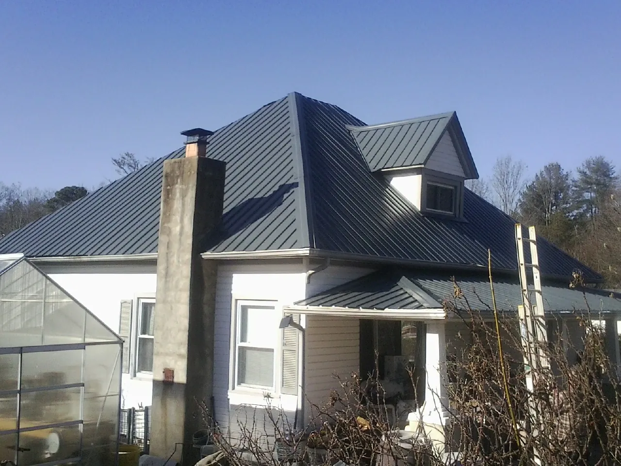 Dark blue standing seam metal roof on a white farmhouse with dormer — Slate & Tile Roof Repair by Roofing Brothers in Merrill