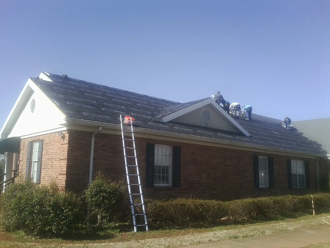 Crew tearing shingles off a brick ranch roof with a ladder set — Emergency Roof Repair work by our crew in Merrill
