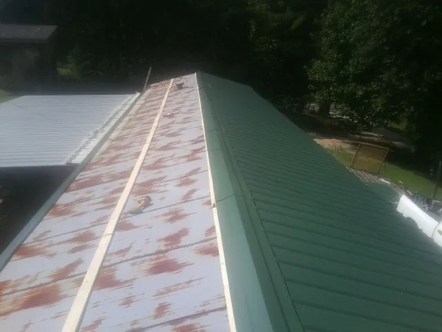 Old rusted panels beside newly installed green metal roofing — Wind Damage Roof Repair by Roofing Brothers in Merrill