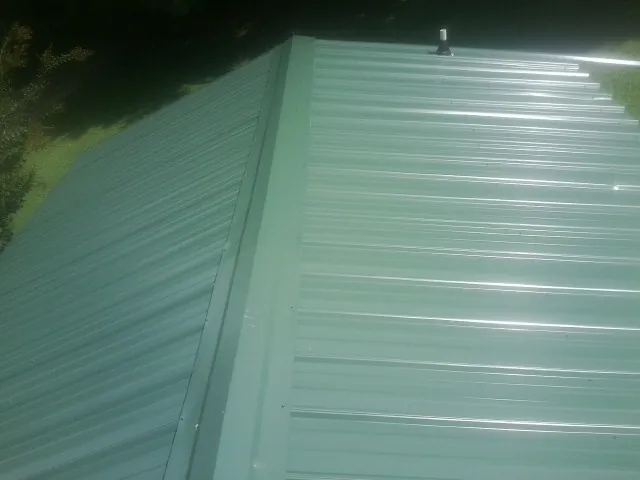 New green metal panels meeting at the ridge of a roof — Flat Roof Repair work by our crew in Merrill