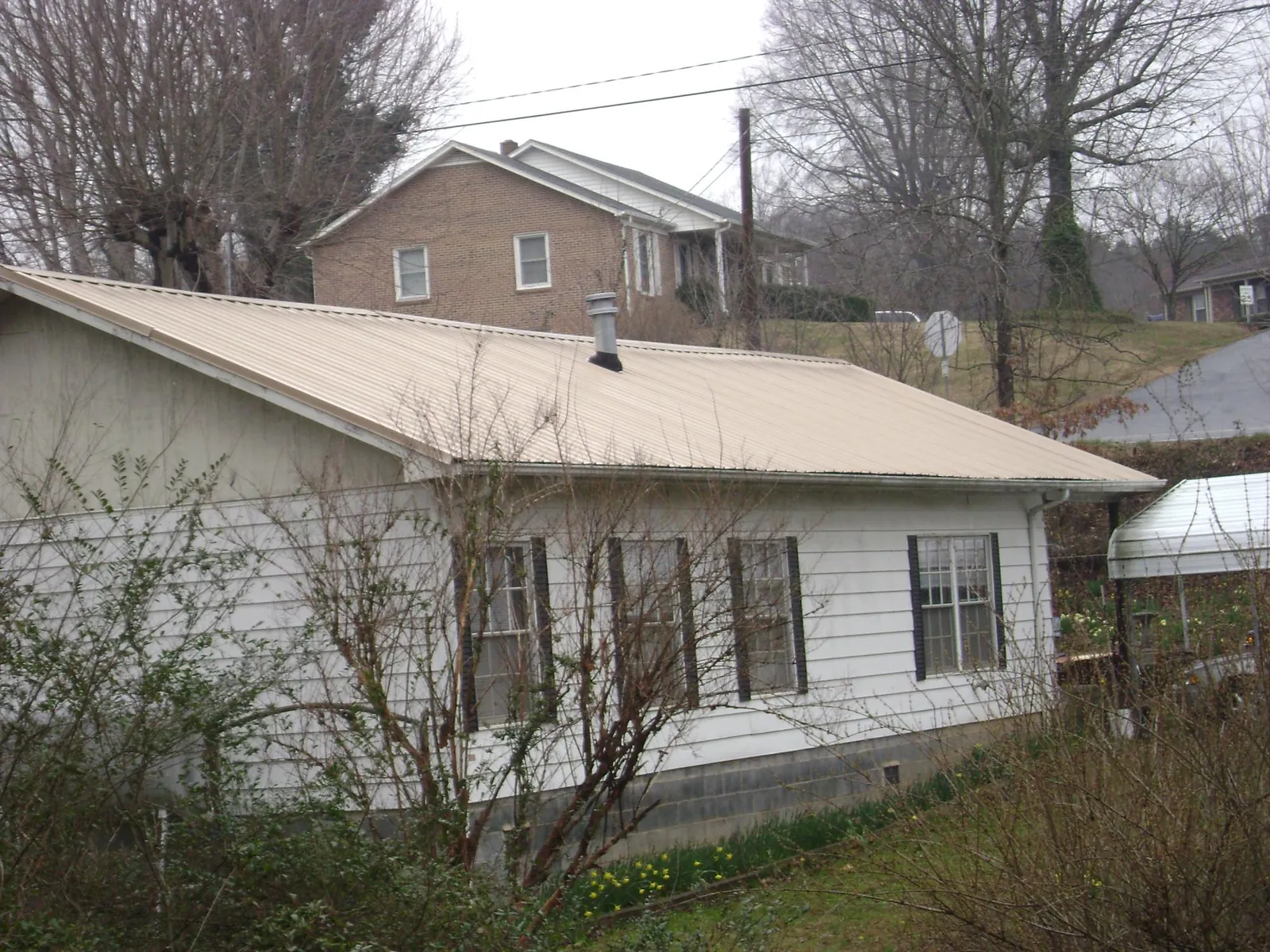 Tan metal roof on a white sided house set into a hillside — Commercial Roofing by Roofing Brothers in Merrill